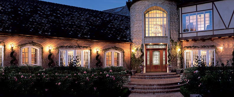 brown Therma-Tru wood appearing door with opaque windows on a grand house at night
