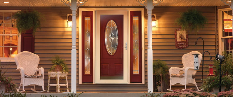 ProViaDoors_StormDoor_792x331 red ProVia door with white accents and special decorative windows in oval and rectangle shapes on porch with white patio chairs