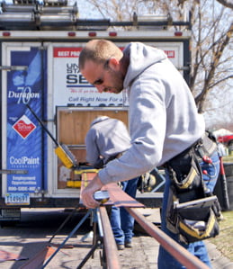 Customer-Focused Engineering and Innovation worker carefully measures section of red United States Seamless Siding on a saw horse outside