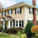 tan home exterior with seamless steel siding, brick-colored roofing, white accents, and chimneys