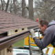 two installers carefully attach fascia to a roof with dark brown shingles