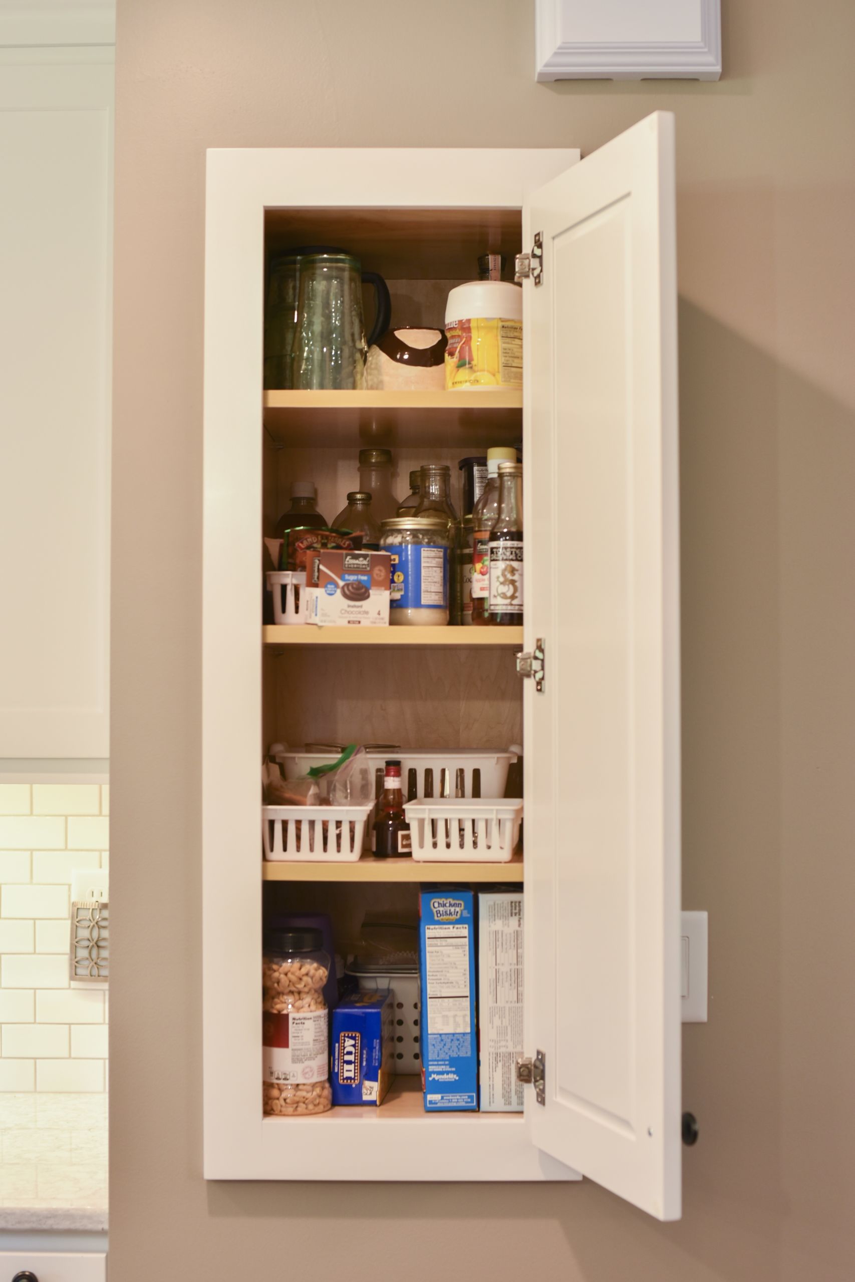 small, white, recessed wall cabinet filled with food items
