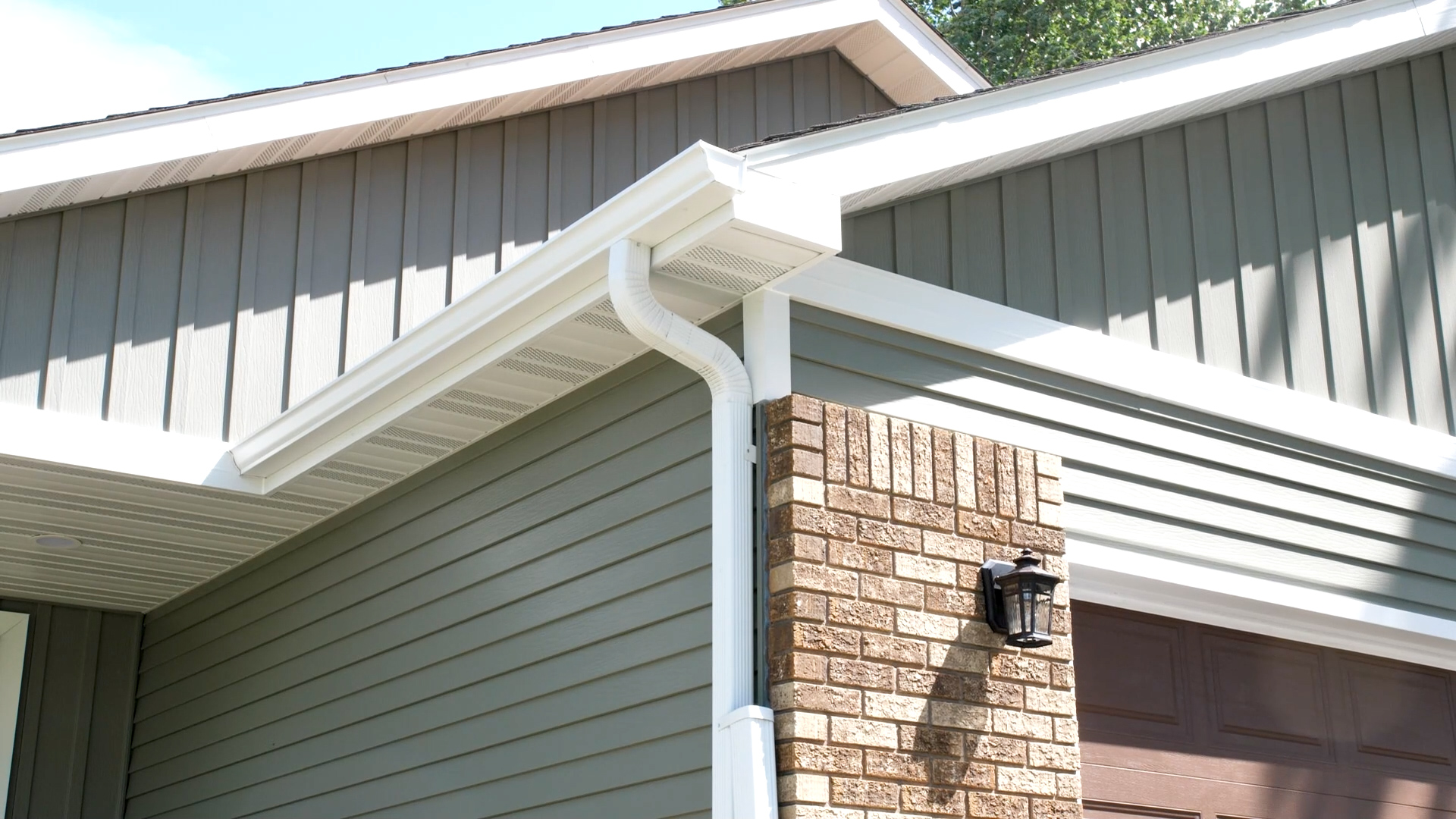 Close-up of a home exterior with gray seamless steel siding, white trim, and brick accents.