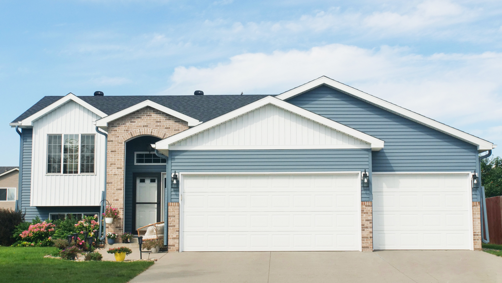 Home exterior with pale blue seamless steel siding, white trim and garage doors, and brick accents.