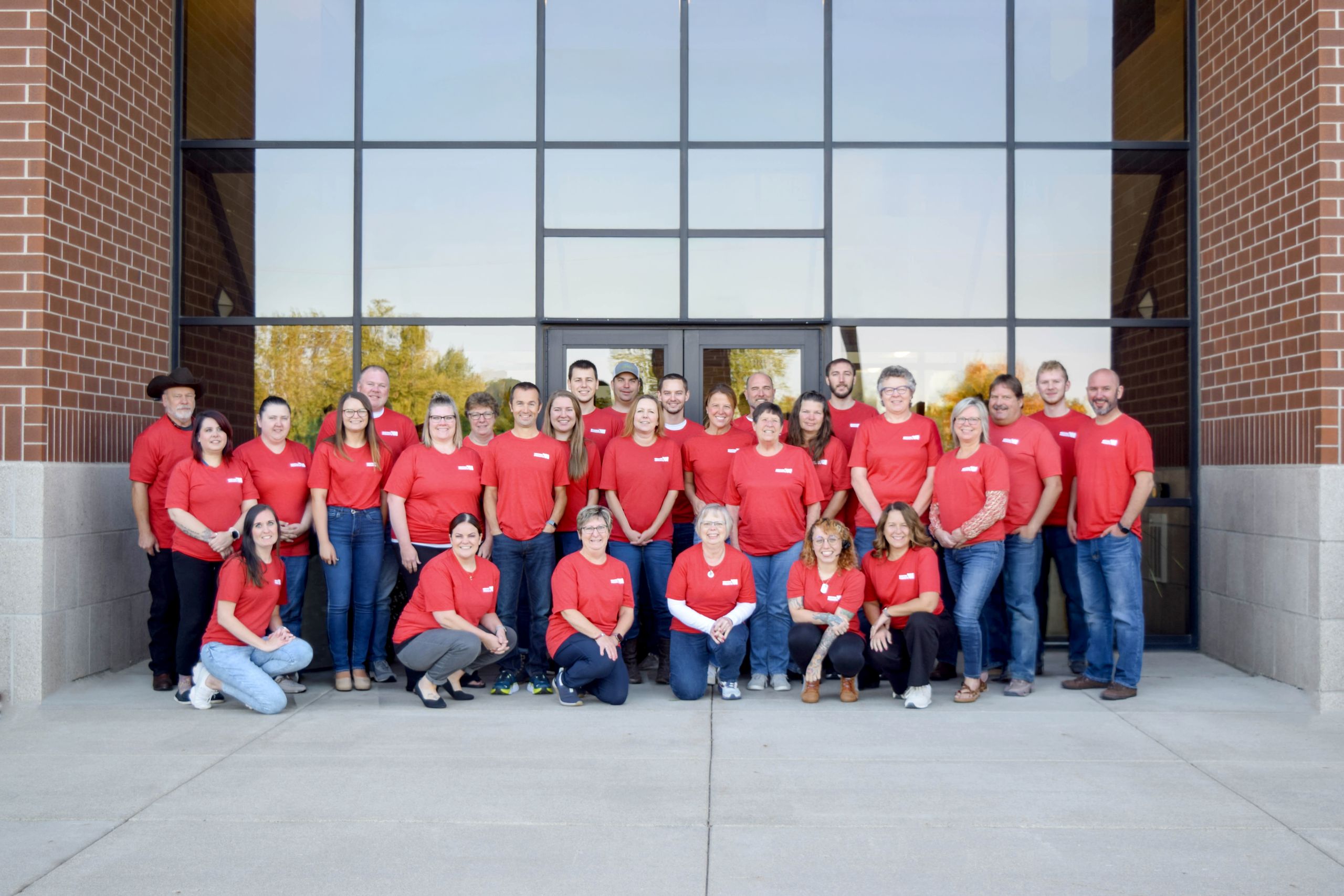 Group of Western Products employees wearing red shirts and posing in front of the company's office building entrance.